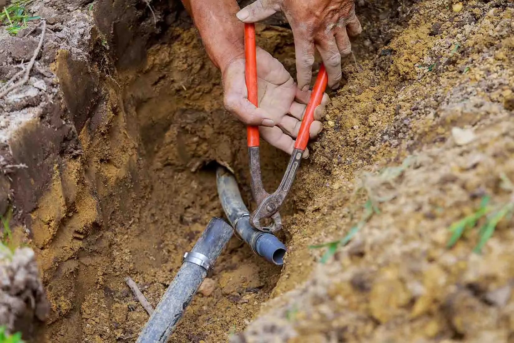 Technician repairing a buried irrigation line in an open trench